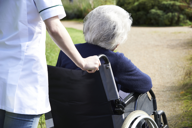 Close Up Of Carer Pushing Senior Woman In Wheelchair carer